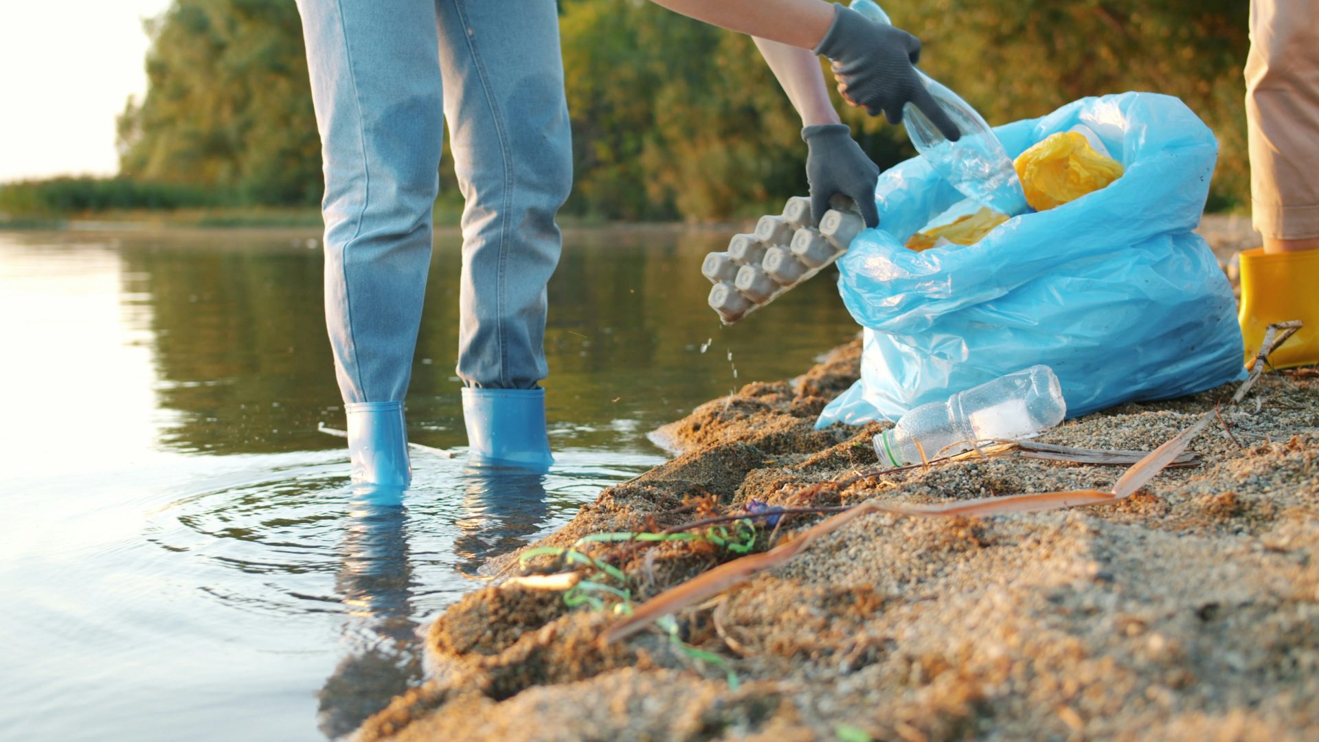 People cleaning trash from a riverbank with a blue bag.